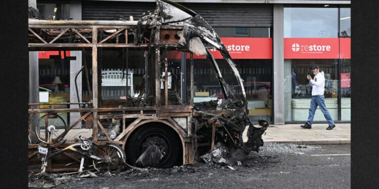 A pedestrian passes a burned-out bus Wednesday following a night of anti-immigrant riots Tuesday in Belfast, Northern Ireland.