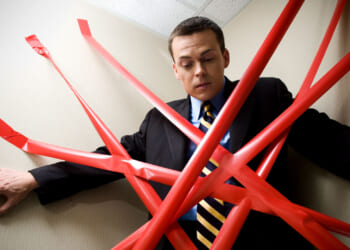 Man in a suit pinned in a corner by numerous strips of red tape.