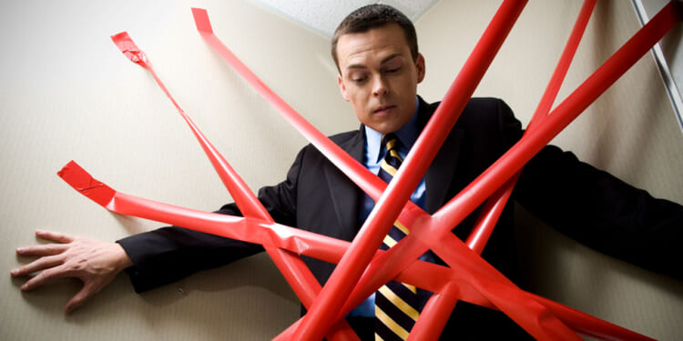 Man in a suit pinned in a corner by numerous strips of red tape.