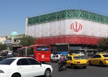 Traffic moves past the Iranian national flag displayed on a building at Enghelab square in Tehran on June 14, 2026.