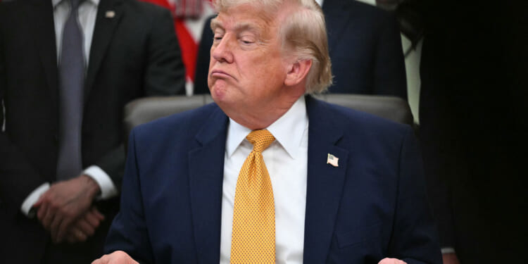 A frowning President Trump sits at his Oval Office desk.