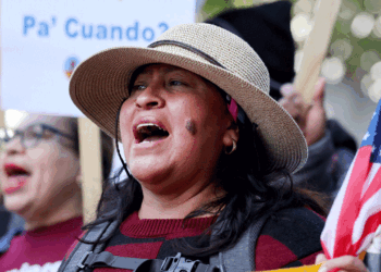 A hispanic woman protests in the street while holding an American flag.