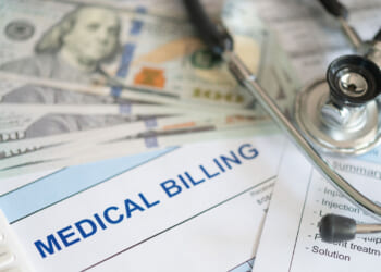 A fanned-out batch of $100 bills on top of a bill reading "Medical Billing" next to a stethoscope.