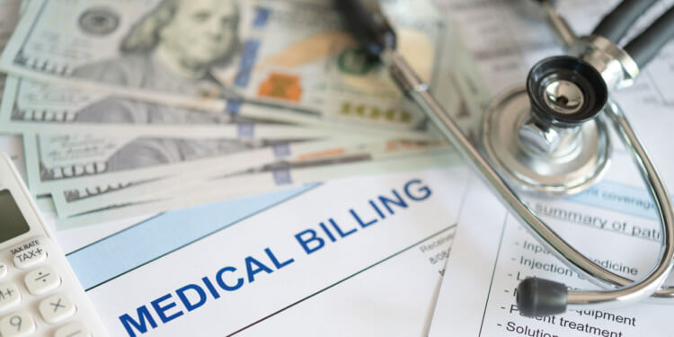 A fanned-out batch of $100 bills on top of a bill reading "Medical Billing" next to a stethoscope.