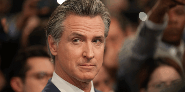 Newsom stands in an audience, looking to the side.