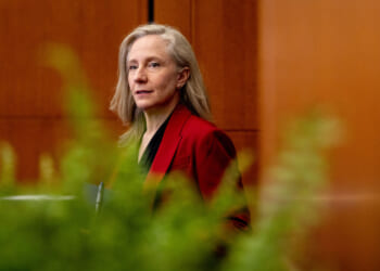 Gov. Abigail Spanberger in red jacket, seen through a row of marijuana plants in the foreground.