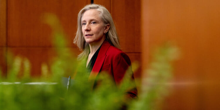 Gov. Abigail Spanberger in red jacket, seen through a row of marijuana plants in the foreground.
