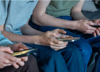 Three teen boys are seen looking at their smart phones.