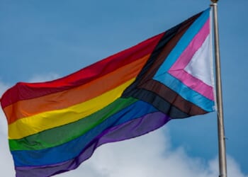A rainbow flag flies against a blue sky.