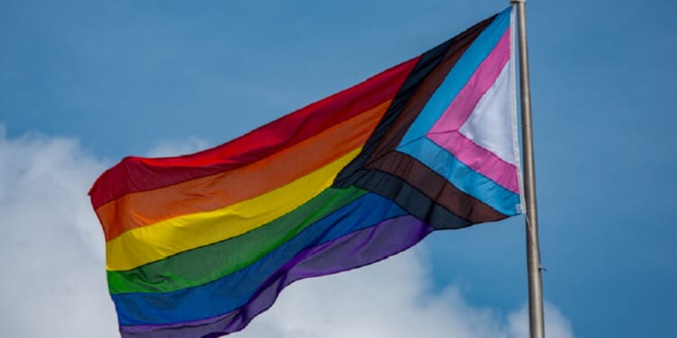 A rainbow flag flies against a blue sky.