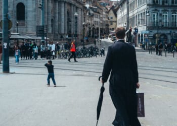 A priest walking in the street in a cassock holding an umbrella and a paper bag, in Besancon, Doubs department, France, on June 22, 2024.