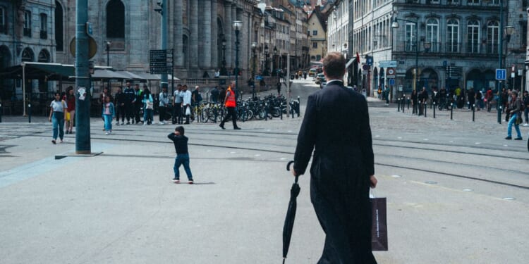 A priest walking in the street in a cassock holding an umbrella and a paper bag, in Besancon, Doubs department, France, on June 22, 2024.