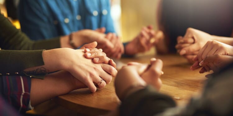 A group holds hands in a prayerful position.