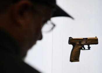 Silhouette of man looking at a display of a handgun against a white background.