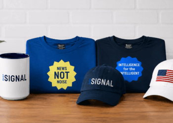 Daily Signal T-shirts, coffee mug, and hats on a table with a white brick background.