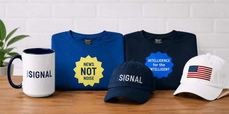 Daily Signal T-shirts, coffee mug, and hats on a table with a white brick background.