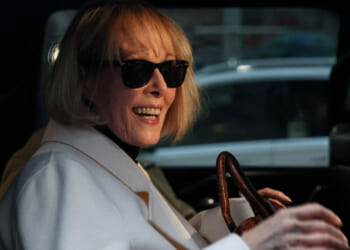 Close-up of E. Jean Carroll in sunglasses and white coat smiling while seated in car.