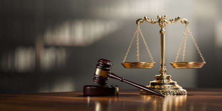 A gavel and wooden block sit alongside a balancing scale in a room flooded with light.