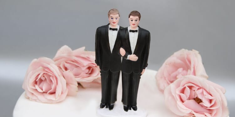 A wedding cake with a decoration showing two grooms on top of it.