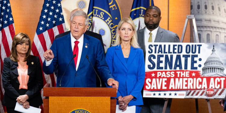 Rep. Ralph Norman of South Carolina Stands at the center of a podium, while other members and a sign urging passage of the SAVE America Act are beside him.