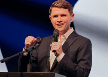 James Talarico with one hand clenched and the other holding a mic, speaks at a podium.