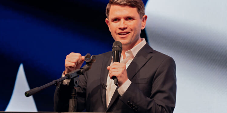 James Talarico with one hand clenched and the other holding a mic, speaks at a podium.