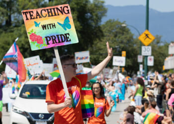 A male teacher carries a sign reading "Teaching With Pride" during a Pride Parade.
