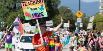 A male teacher carries a sign reading "Teaching With Pride" during a Pride Parade.