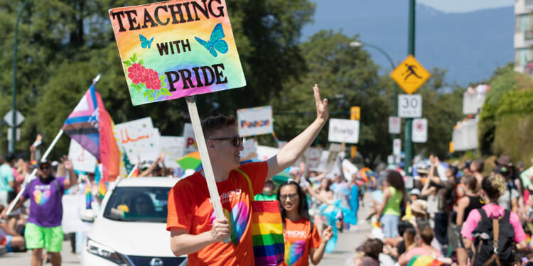 A male teacher carries a sign reading "Teaching With Pride" during a Pride Parade.