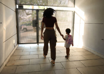 Young black woman leads child toward outside door.