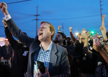 A crowd of mostly white protesters raise fists in air.