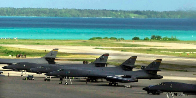 American fighter planes sit on a runway at Diego Garcia base with beautiful blue island waters in background.