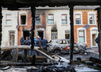 People stand next to burnt-out cars and homes Wednesday after demonstrations turned violent the night before in eastern Belfast, Northern Ireland.