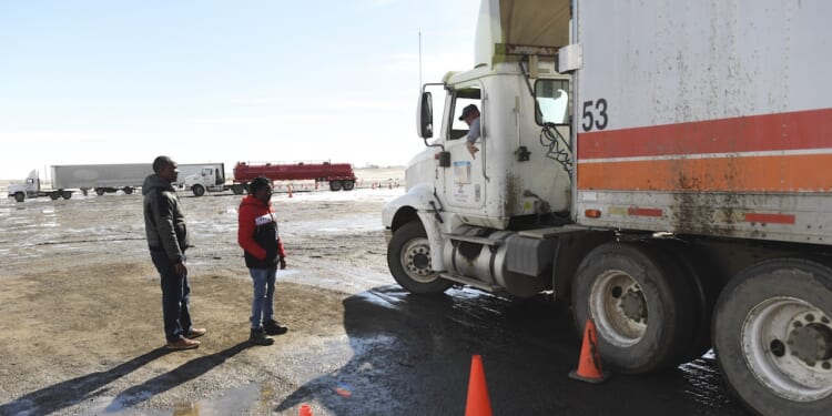 Immigrants stand and look at a truck as they learn how to backup an 18-wheeler.