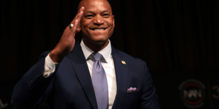 Maryland Gov. Wes Moore raises hand toward forehead as if about to salute.