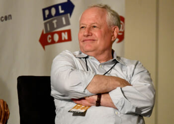 Bill Kristol sits with his arms folded while in a white shirt.