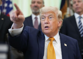 President Trump points with his left hand while sitting in the Oval Office.