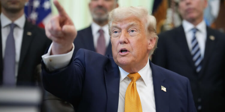 President Trump points with his left hand while sitting in the Oval Office.