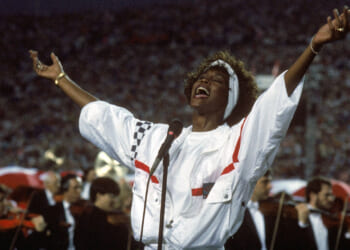 Whitney Houston in a white, with blue and red trim pullover, has her arms outstretched as she concludes singing "The Star-Spangled Banner" during Super Bowl XXV