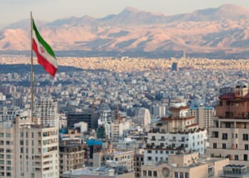 Tehran’s skyline is pictured with a large Iranian flag flying in the sky during sunset.