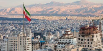 Tehran’s skyline is pictured with a large Iranian flag flying in the sky during sunset.