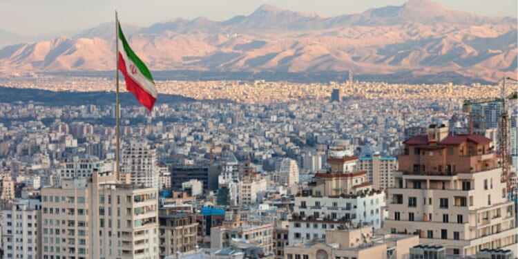 Tehran’s skyline is pictured with a large Iranian flag flying in the sky during sunset.