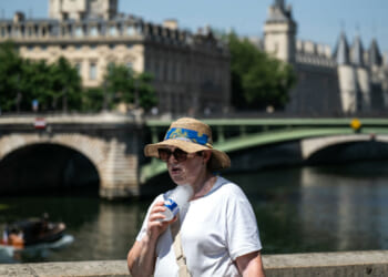 A woman with a hat cools off with a cold bottle of water on the Seine riverside with the Paris commercial court (L) and the Conciergerie buildings and the Pont Notre Dame in the background as France experiences a heat wave in Paris, France, on June 21, 2026.