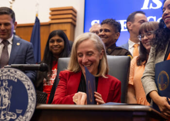 A smiling Abigail Spanberger sits at a desk signing gun control legislation.