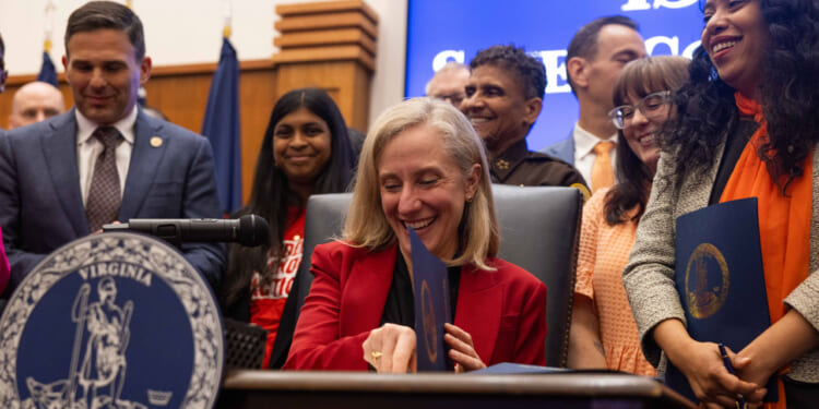 A smiling Abigail Spanberger sits at a desk signing gun control legislation.