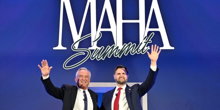 Two men in suits stand side by side, smiling and waving, in front of a blue backdrop with large white text that says “MAHA Summit.”.