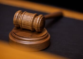 A wooden gavel sits on a wooden block on a black suede desk.