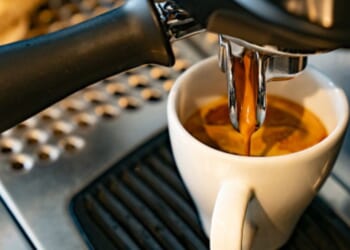 Coffee flows into a white cup from a machine.