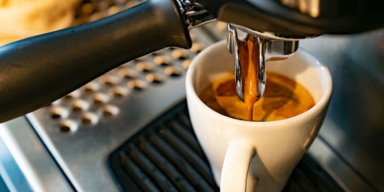 Coffee flows into a white cup from a machine.