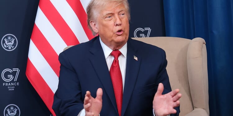Trump in a dark suit and red tie sits in a beige chair, gesturing with his hands. Behind him are a partial U.S. flag and banners with G7 France 2019 and the U.S. State Department seal.